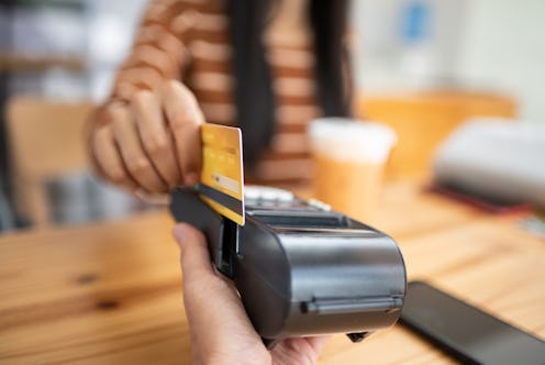 Young asian woman paying her order by credit card on payment terminal in coffee shop.