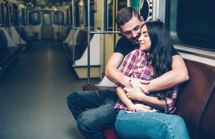 Young man and woman use underground. Couple in subway. Sitting on bench and embrace each other. Happ...