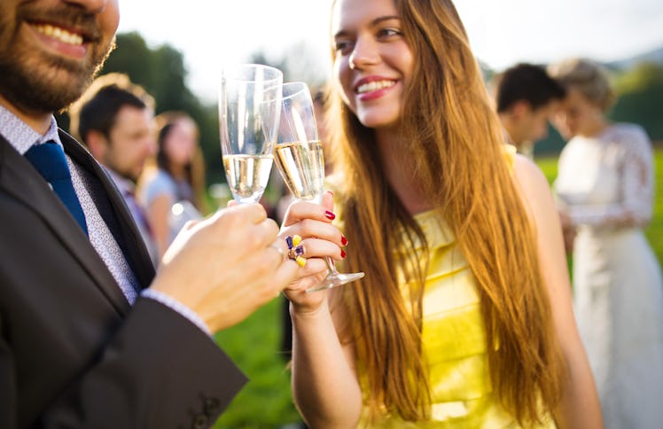 Wedding guests clinking glasses while the newlyweds hugging in the background