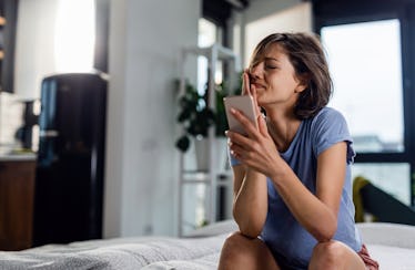 Sad woman crying while sitting on the bed and receiving bad news over the phone. 