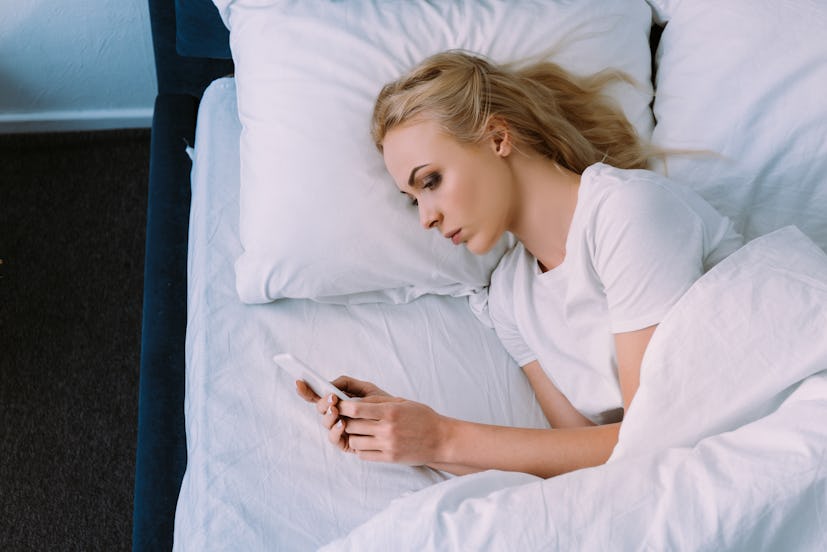 sad lonely woman lying in bed and using smartphone