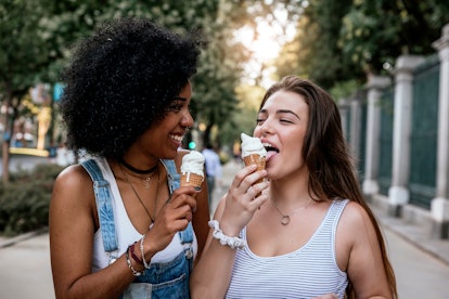 Two girls eat pumpkin ice cream cones while walking in the city.