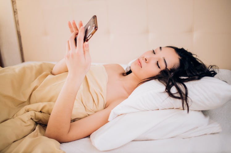 Photo of relaxed woman with black hair watches online story on cell phone, reads post with interesti...