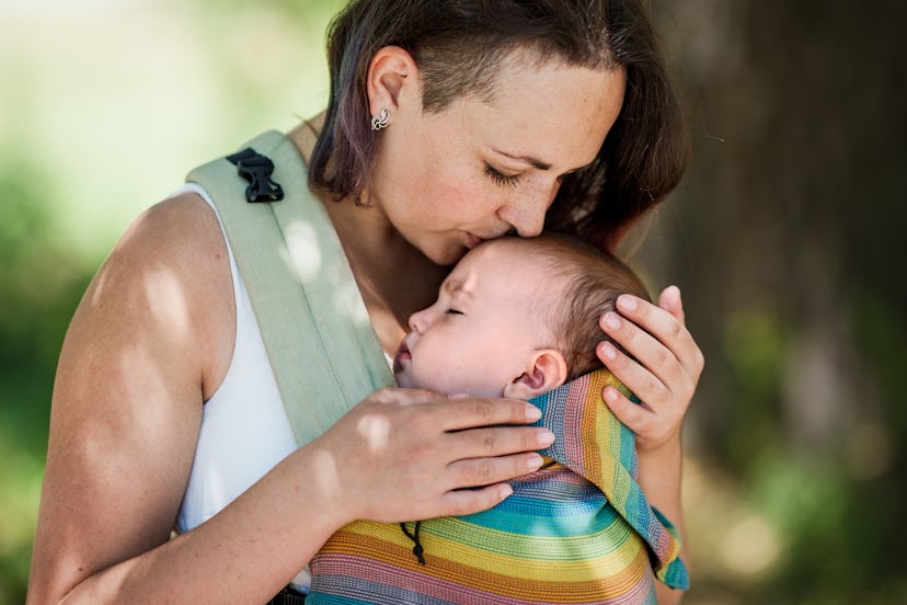 Informal mother carry baby girl in baby carrier in park. Summertime. Concept of natural parenting, b...