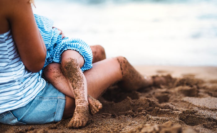A midsection of mother breasfeeding toddler daughter on beach on summer holiday.