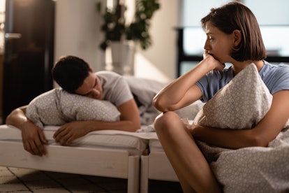 Young sad woman feeling lonely while her boyfriend is sleeping in the bedroom.