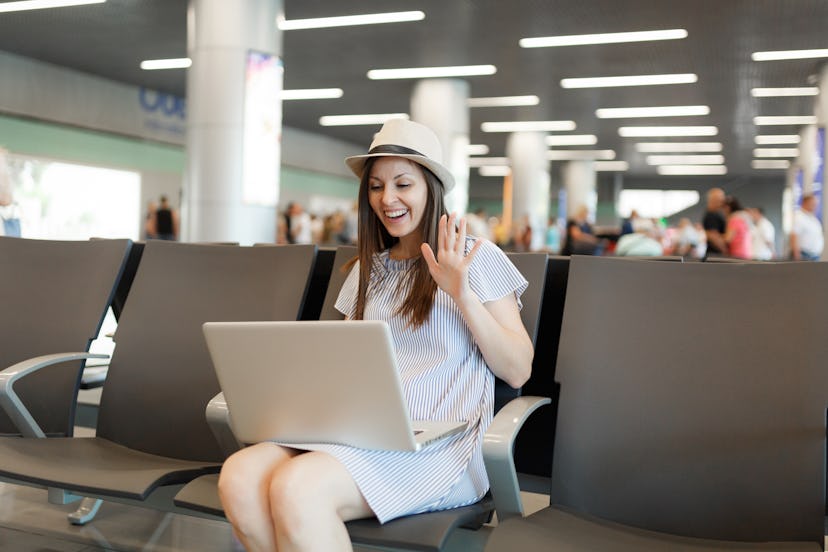 Young traveler tourist woman working on laptop, wave hand for greeting in web-camera during video ca...