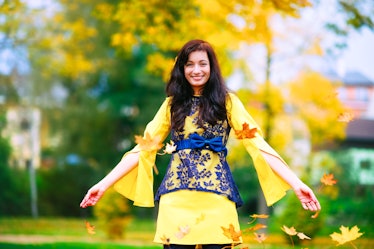 Happy and cheerful girl has a fun with leaves in a fall season. She wears a nice colorful dress. Emo...