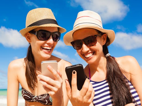 Pretty girls using smart phone on the beach. Summer holiday, technology and beach concept.