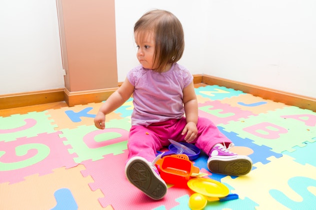 Adorable baby girl sitting on floor mats playing with toys and looking to the side