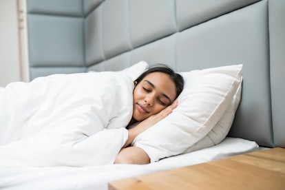 attractive woman sleeping on pillows under blanket in bed