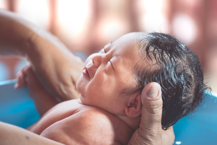 Cute asian newborn baby girl take a bath in bathtub. Mom cleaning her baby body with tenderness