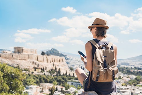 Young woman using smart phone in Athens with Acropolis at the background. Traveler girl enjoying vac...