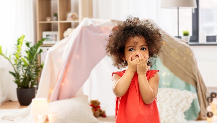childhood, expressions and emotions concept - confused little african american girl covering mouth b...