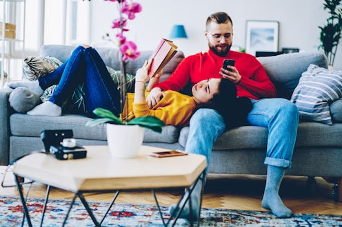 Concentrated man sending text message on smartphone using home wifi on leisure while his girlfriend ...