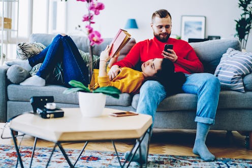 Concentrated man sending text message on smartphone using home wifi on leisure while his girlfriend ...