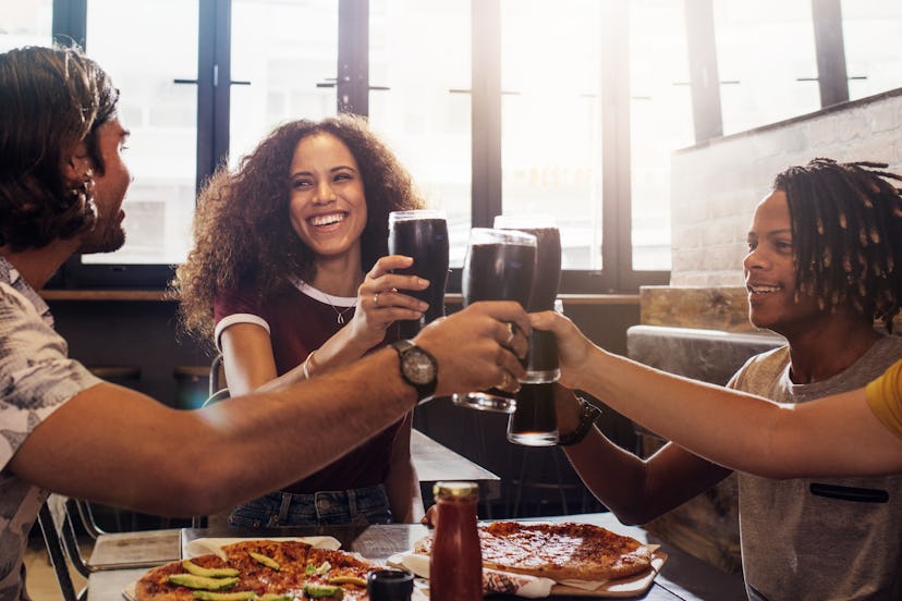 Smiling young men and women sitting inside a restaurant toasting soft drinks. Multi-ethnic group of ...