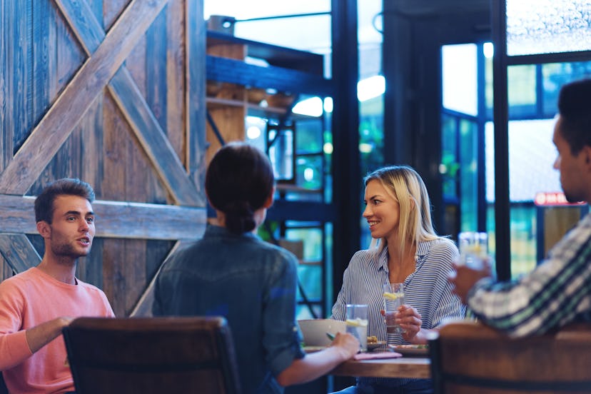 Four friends sitting at wooden table in restaurant and talking over dinner, young man telling story