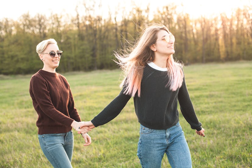 Two young women are walking on the field under sunlight.