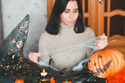 Young woman getting ready for halloween and keeps fake spiderweb among holiday decorations and eleme...