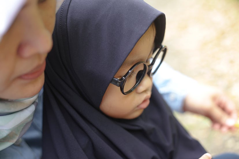 Portrait of happy Asian muslim mom and baby girl daugther talking and playing in the park, blurred w...