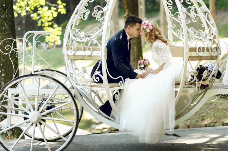 Handsome groom kissing blonde beautiful bride in magical fairy tale carriage in sunlit park