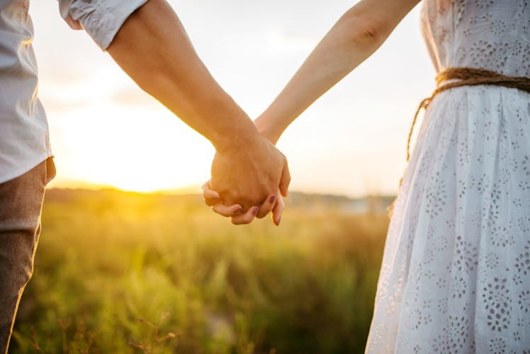 Couple hold hands in green field on sunset