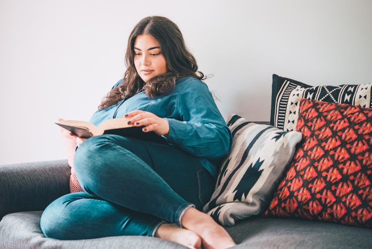 Beautiful plus size girl sitting on sofa reading a book. Toned picture