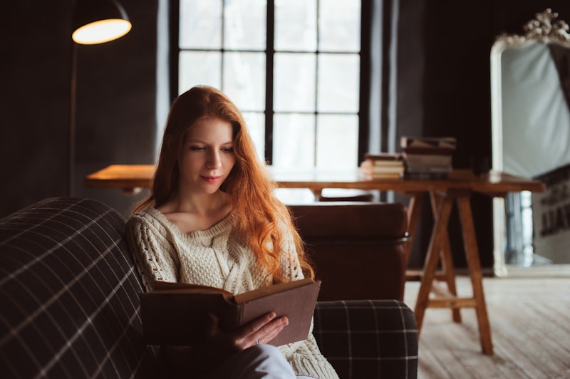 young beautiful redhead woman relaxing at home in the autumn cozy evening and reading book on couch