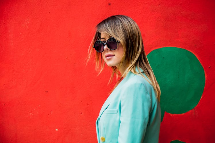 Young woman in Blazer of 90s style and sunglasses in red background.