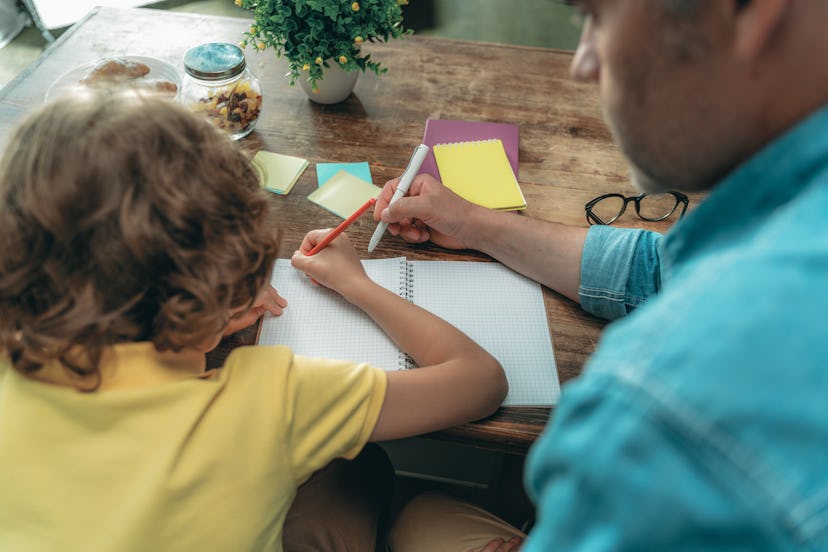 Mature father with little son writing in copybook and making school homework