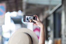 A woman wearing a hat is taking a selfie using her cell phone. Women taking a selfie on the footpath...