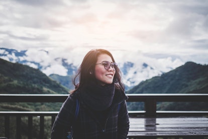 Portrait of smiling Asian woman wearing sunglasses with foggy forest view and breathtaking mountain ...