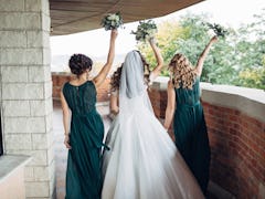 Look from behind at bride and bridesmaids in green dresses dancing on the balcony