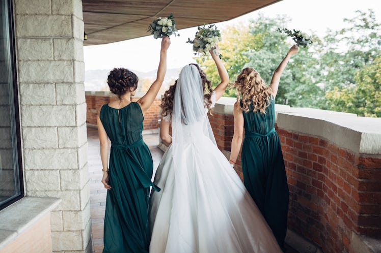 Look from behind at bride and bridesmaids in green dresses dancing on the balcony
