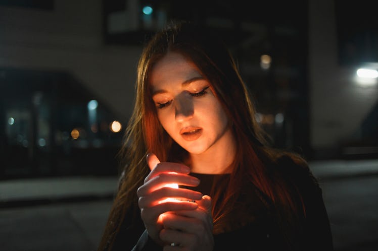 Young redhead woman with a burning lighter in the night city.