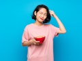 Asian young woman holding a bowl of cereals having doubts and with confuse face expression