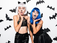 Picture of two emotional young women in halloween costumes on party over white background. Looking c...