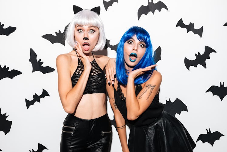 Picture of two emotional young women in halloween costumes on party over white background. Looking c...