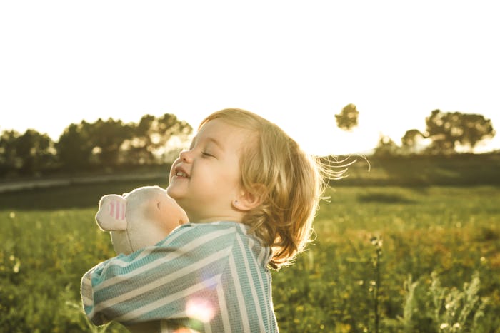 Happy little girl playing with a stuffed animal on the field. Kid hugging a teddy bear.