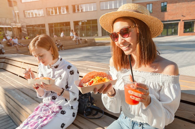 Two girls eat traditional Mexican fast food tacos and drink michelada on the street. Communication a...