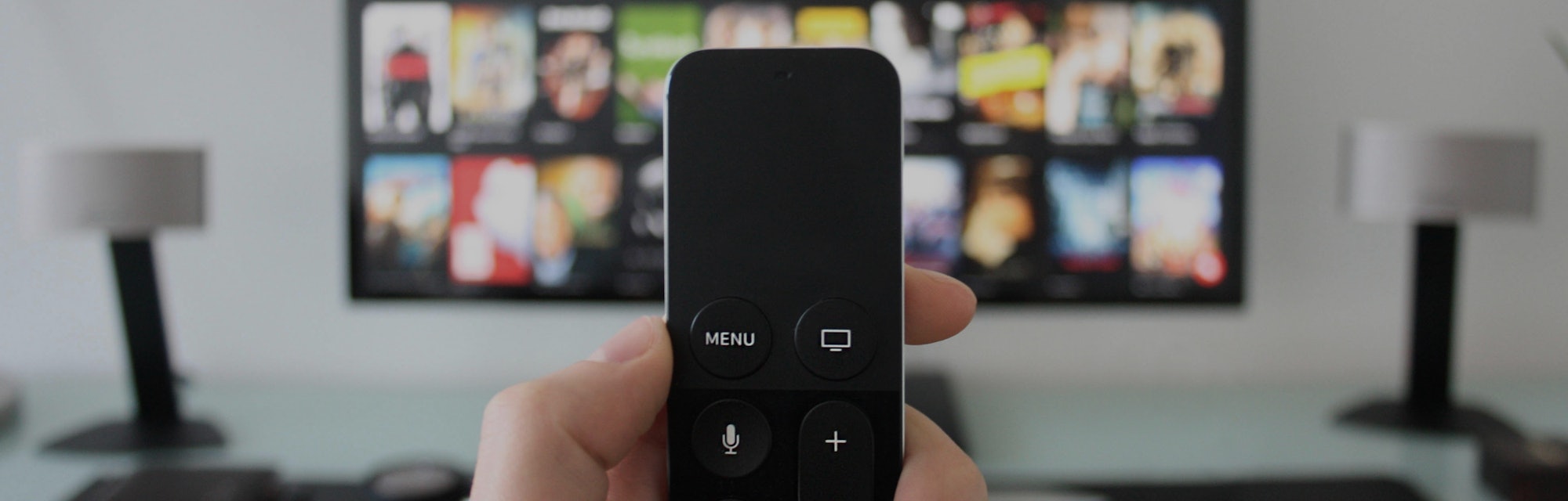 Hand holding a TV remote while watching shows on a streaming service on Television.