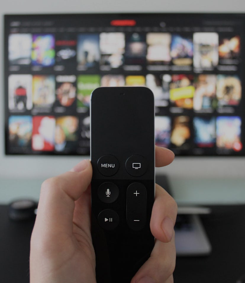 Hand holding a TV remote while watching shows on a streaming service on Television.
