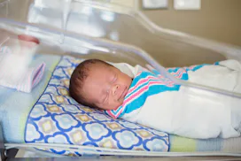 Sleeping baby boy resting in a hospital crib in a hospital delivery room. The ethnically diverse chi...