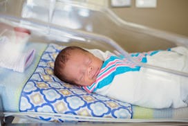 Sleeping baby boy resting in a hospital crib in a hospital delivery room. The ethnically diverse chi...