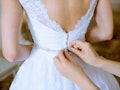 Bridesmaid is lacing white wedding dress for beautiful bride. Beauty model girl in bridal gown for m...