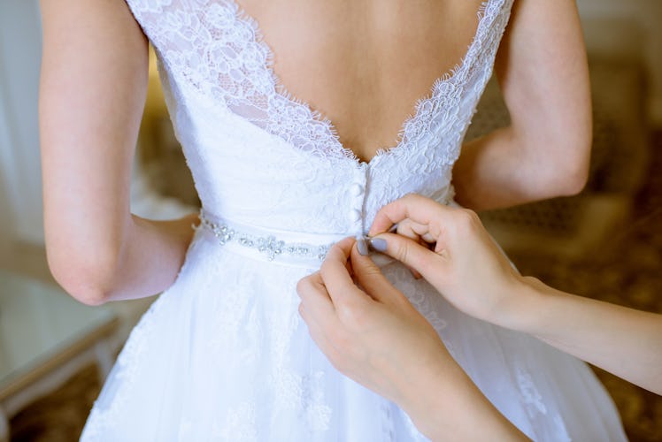 Bridesmaid is lacing white wedding dress for beautiful bride. Beauty model girl in bridal gown for m...