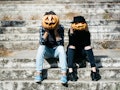 young halloween couple of man and girl or woman in black witch hat in jeans sitting on stony stairs ...