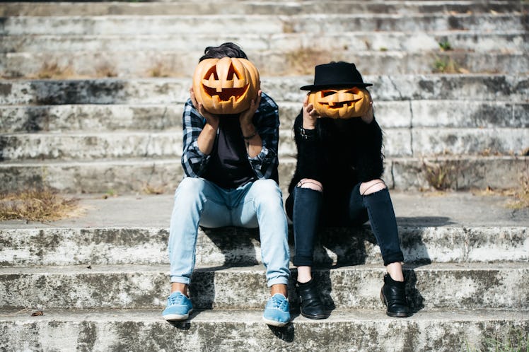 young halloween couple of man and girl or woman in black witch hat in jeans sitting on stony stairs ...