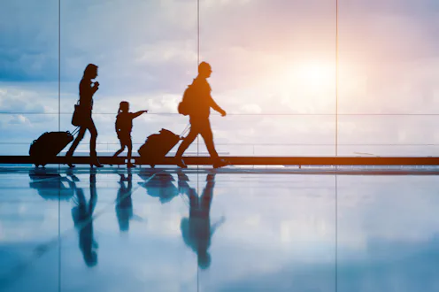 Family at airport travelling with young child and luggage walking to departure gate, girl pointing a...